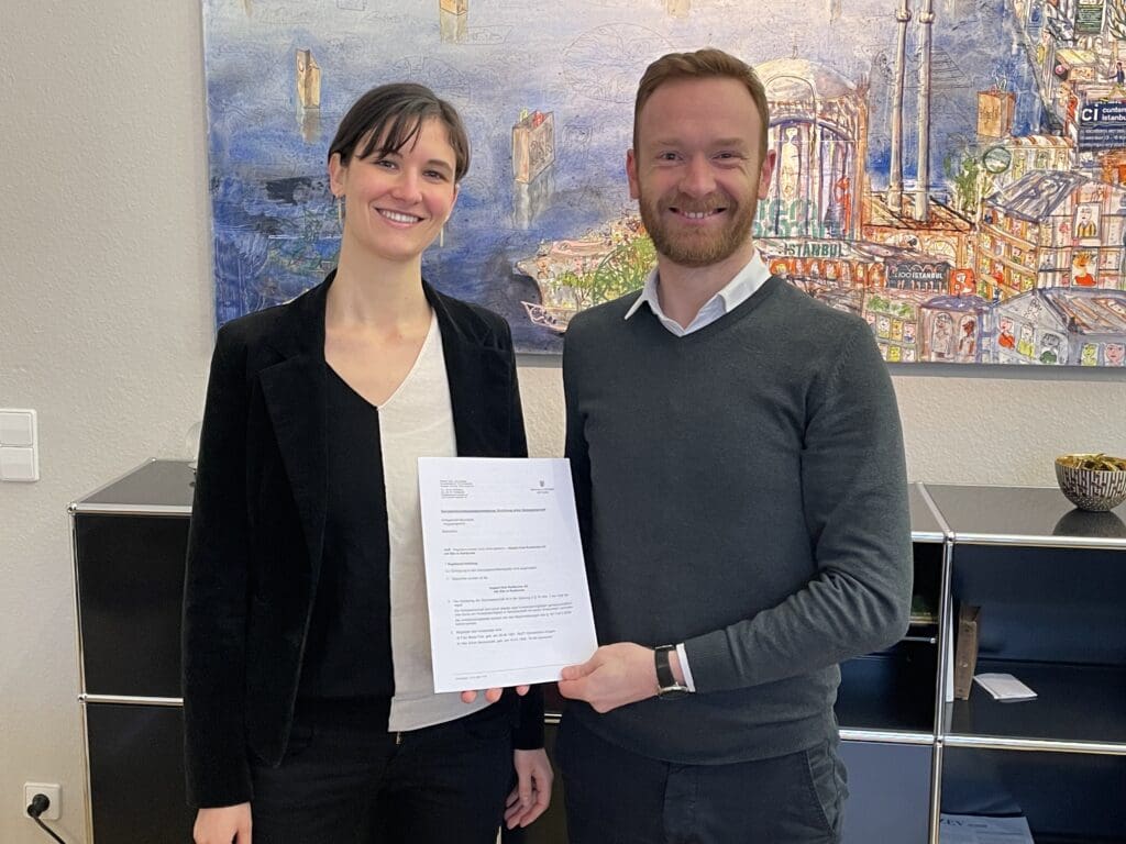 Maria und Anton stehen nebeneinander und zeigen die Genossenschaftsurkunde ins Foto