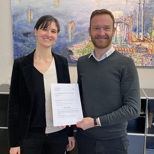 Maria und Anton stehen nebeneinander und zeigen die Genossenschaftsurkunde ins Foto
